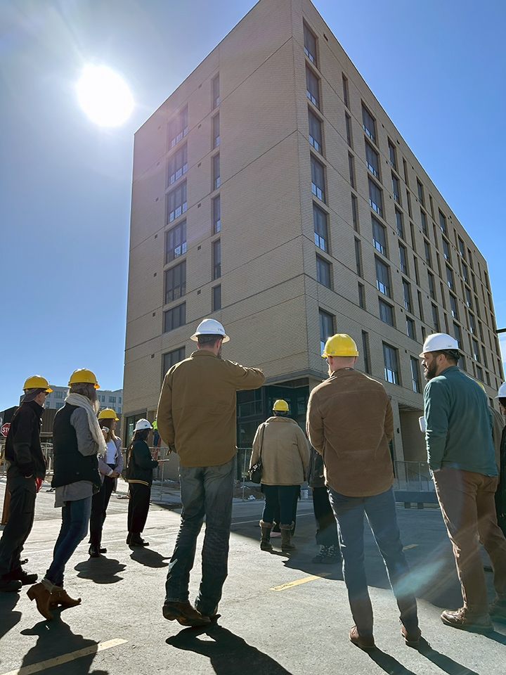 people in construction hats look at a tall apartment building
