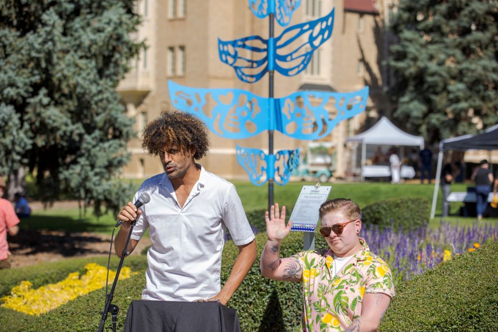 Artists Michael Gadlin and Axel Leonhardt spoke at the Mosaic Community Block Party with their art piece in the background.