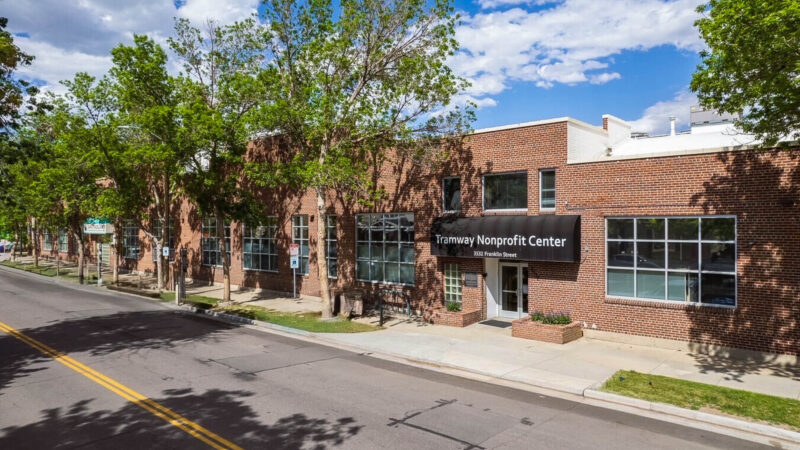 Brick building with trees lining the road, front sign: Tramway Nonprofit Center