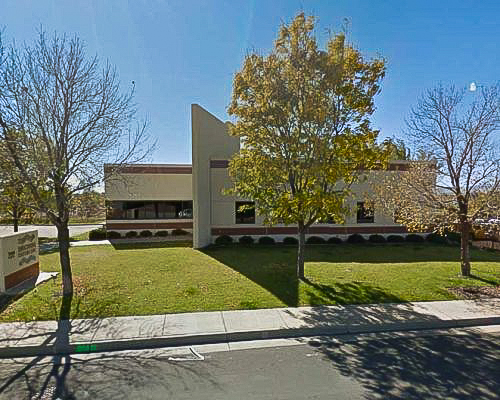 One-story building with visual dividing wall splitting it. Blue sky, green grass.