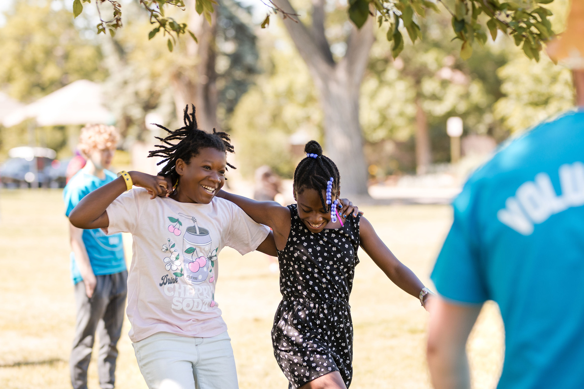 Two girls walking arm in arm outside laughing.