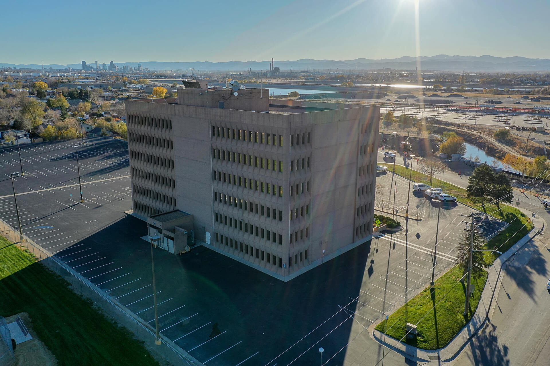 aerial view of 6-story white building surrounded by a parking lot, with sun creating lens flare