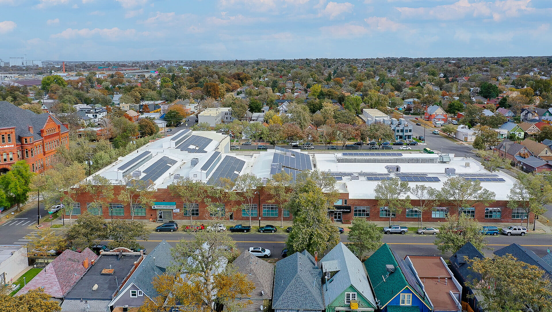 Aerial shot of brick building spanning a block, white roof and solar panels on top