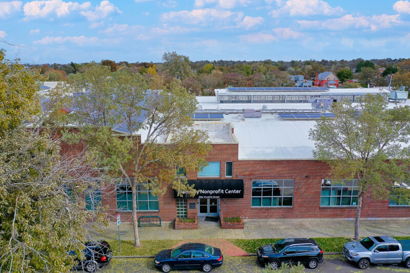 Cars and trees lining the road in front of brick building with sign: Tramway Nonprofit Center