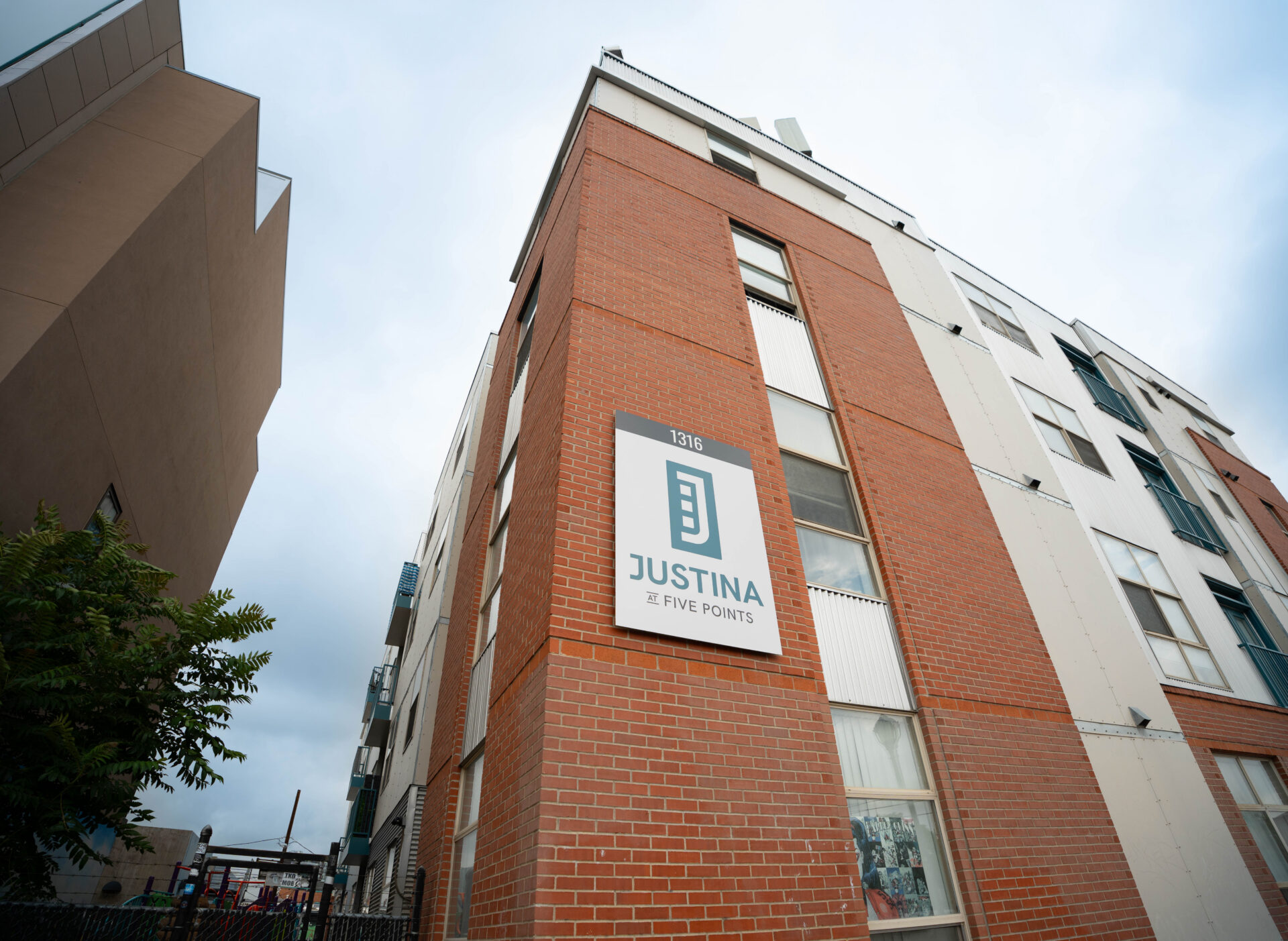 a multifamily brick apartment building with a sign that says Justina at Five Points