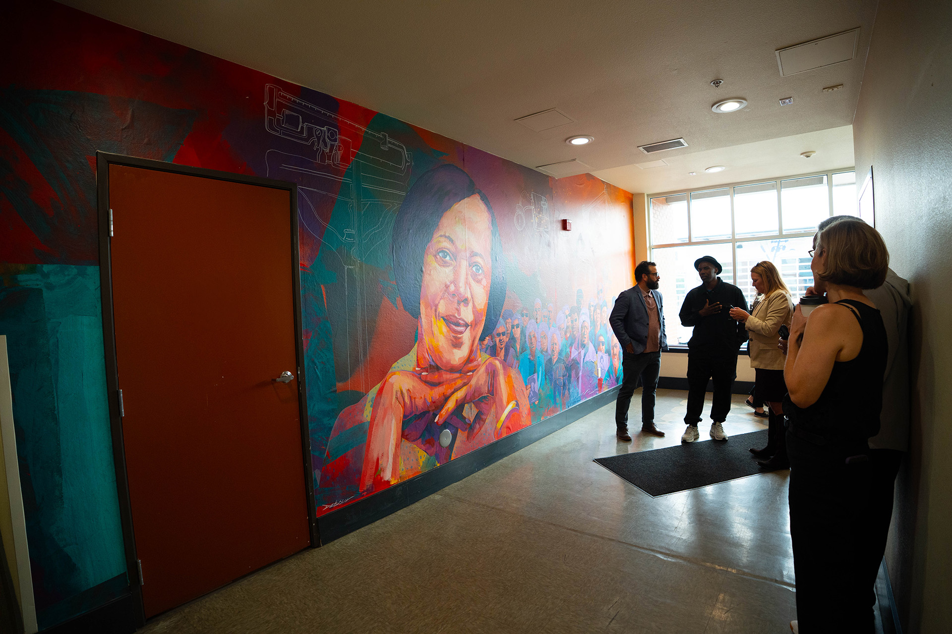 a colorful mural of a woman and community around her, silhouettes of people talking in front of the mural