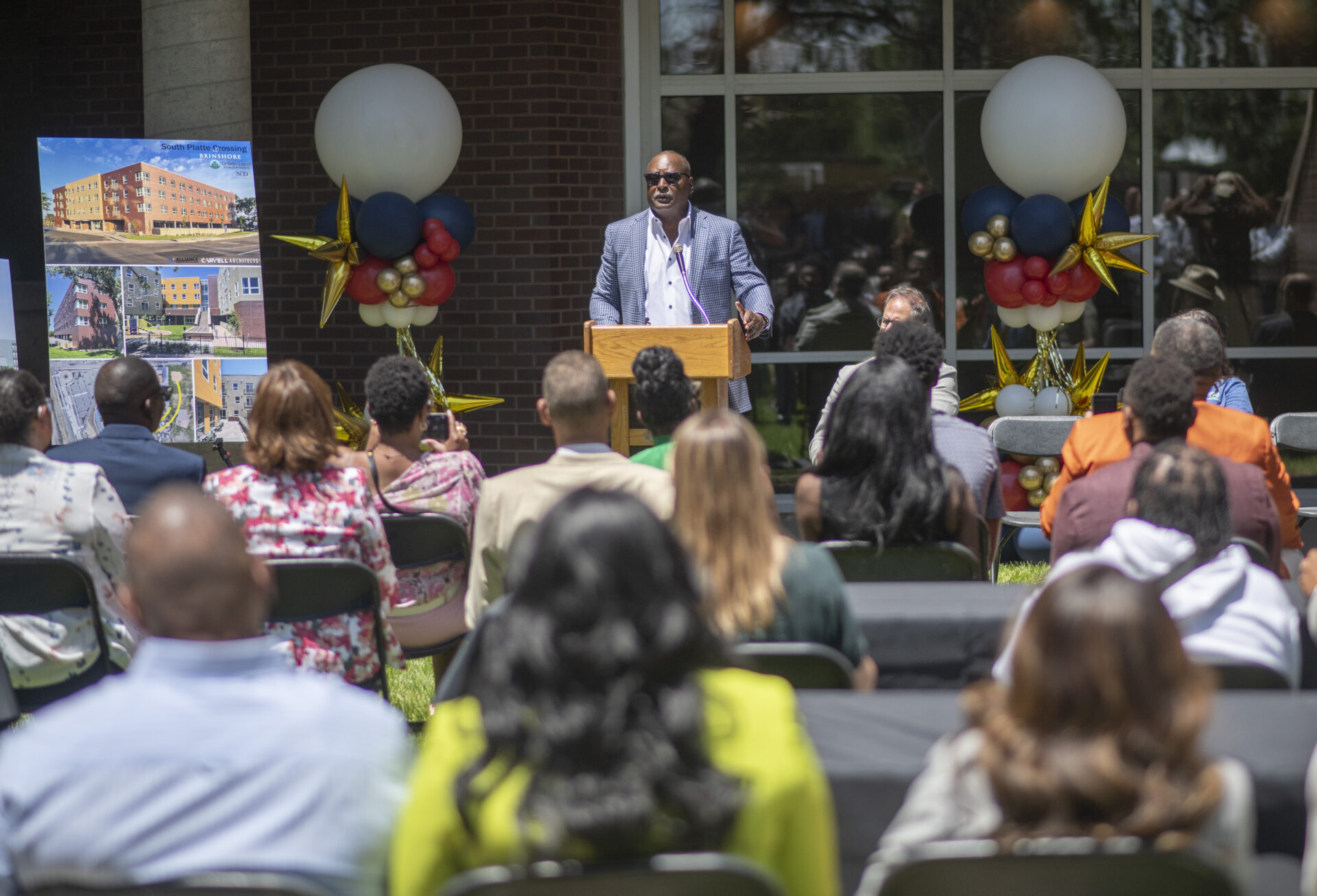 Eric L. Nesbitt, Esq., speaks at the podium during the South Platte Crossing grand opening, addressing attendees about affordable housing and community investment.