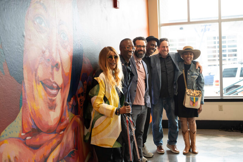 a group of people pose in front of a mural of a woman's face